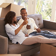 Two people drinking coffee together on the couch with their legs up on a cardboard box