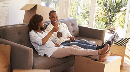 Two people drinking coffee together on the couch with their legs up on a cardboard box