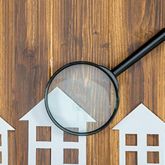 paper cutouts of homes on a wooden table with a magnifying glass