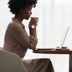 Business person sitting at desk drinking coffee and looking at laptop