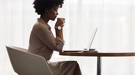 Business person sitting at desk drinking coffee and looking at laptop