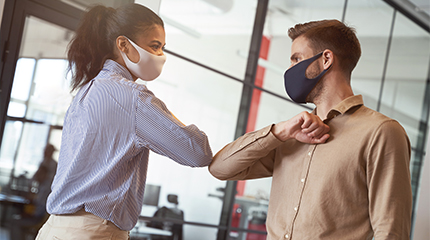 Two employees wearing masks touching elbows