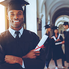 Smiling students on graduation day. They are wearing cap and gown. They are holding diplomas in hand.