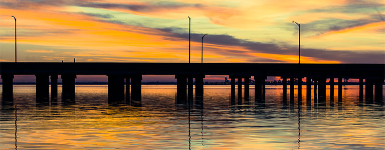 A low bridge stands in front of a Gulf Coast sunset.