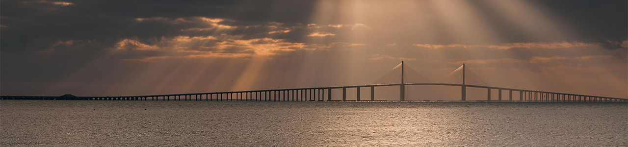Rays of light shine down from a cloudy sky onto a bridge.
