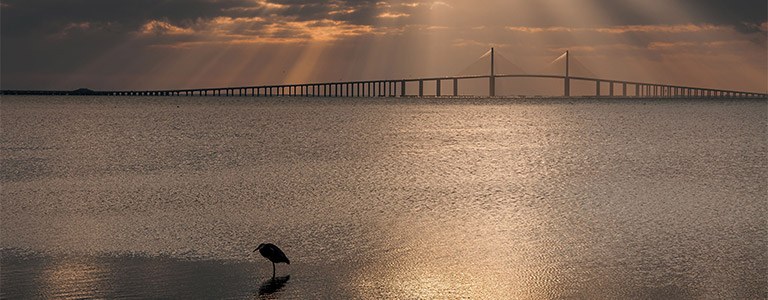 Rays of light shine down from a cloudy sky onto a bridge.