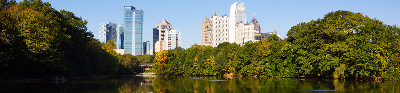 The skyscrapers of downtown Atlanta in front of the forested shore of Piedmont Park.