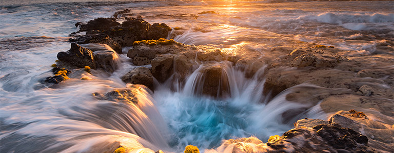 Water flows into a hole on the rocky Hawaiian shoreline.