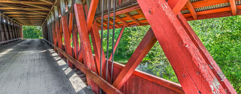 A red wooden bridge hangs over a lush stream.
