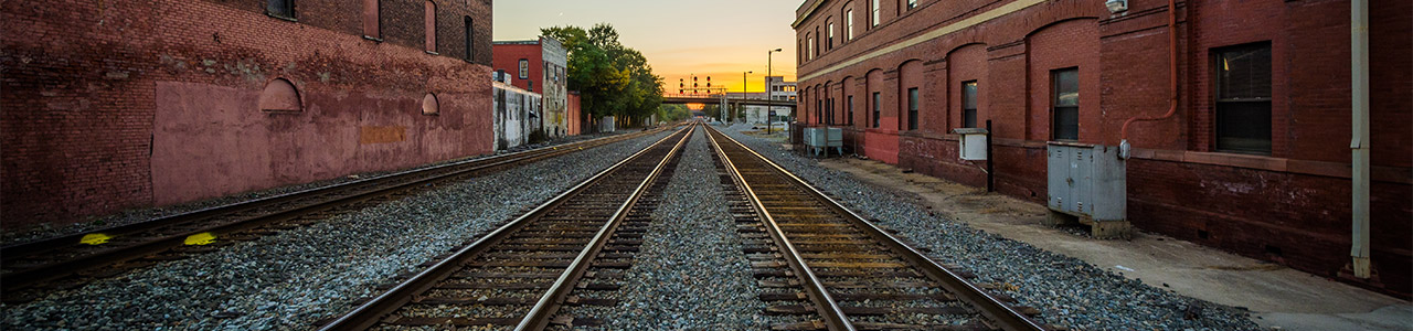 Three railroad tracks stretch into the distance along city blocks.