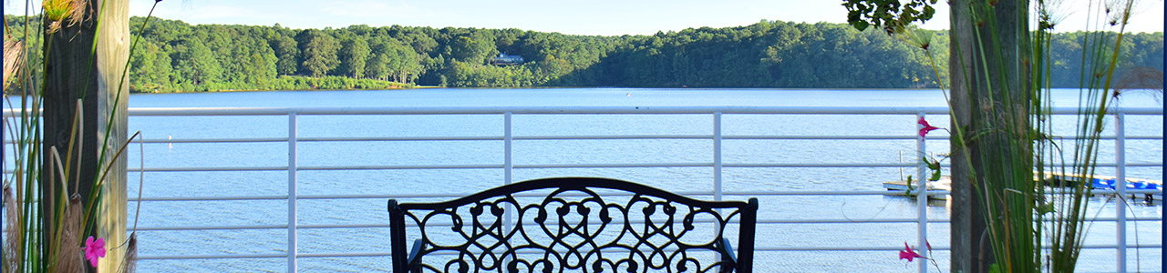 The view looking out from a wooden dock towards a river. The forested shoreline can be seen across the river.