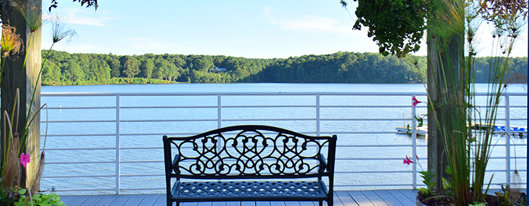 The view looking out from a wooden dock towards a river. The forested shoreline can be seen across the river.