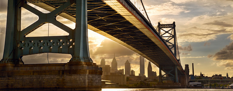 A bridge stretches over a river with downtown Philadelphia in the background.