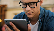 Person wearing glasses looking at tablet held in their hand.